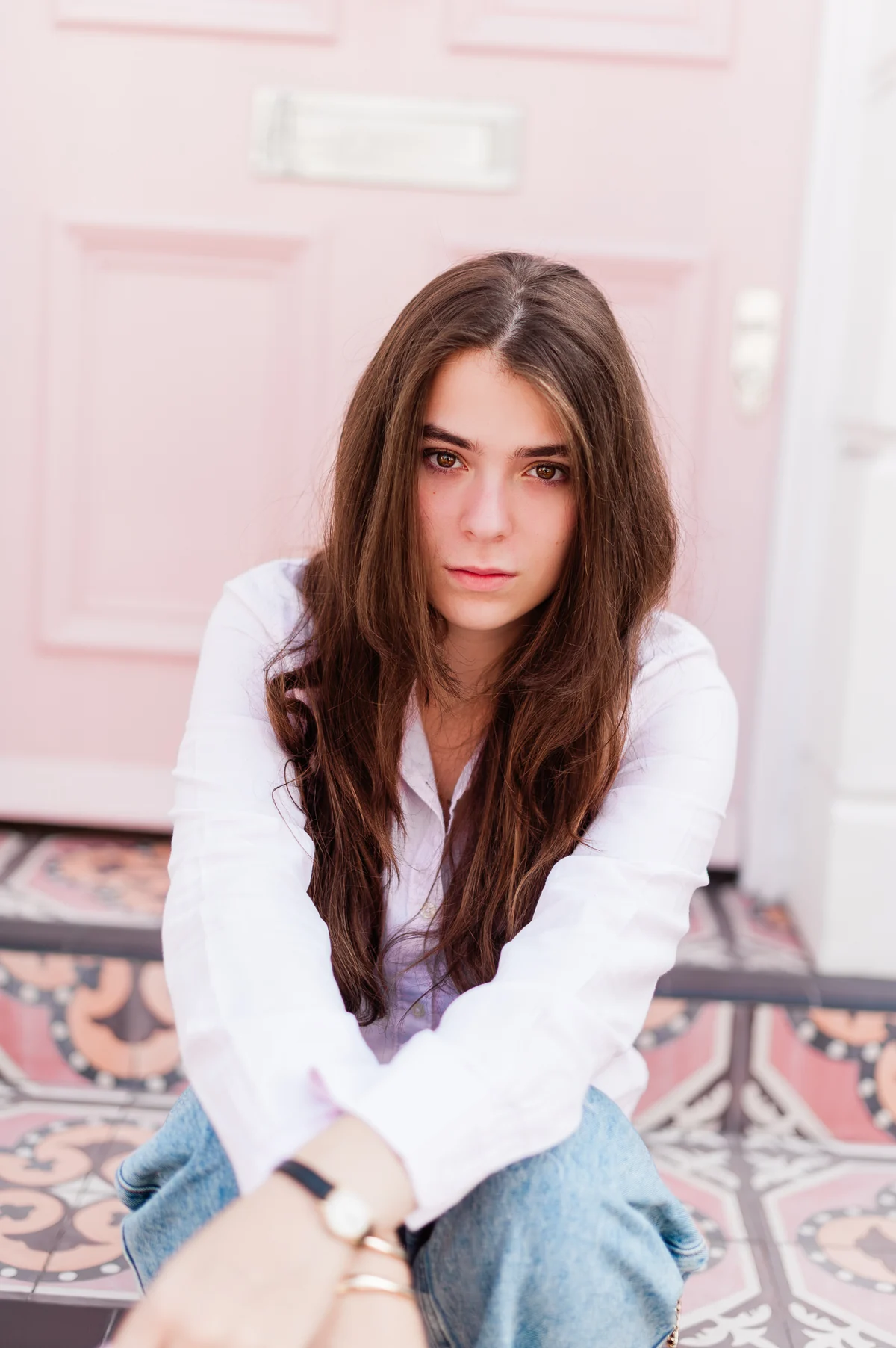 Julia in a white shirt sitting on tiled steps beside a pale pink door
